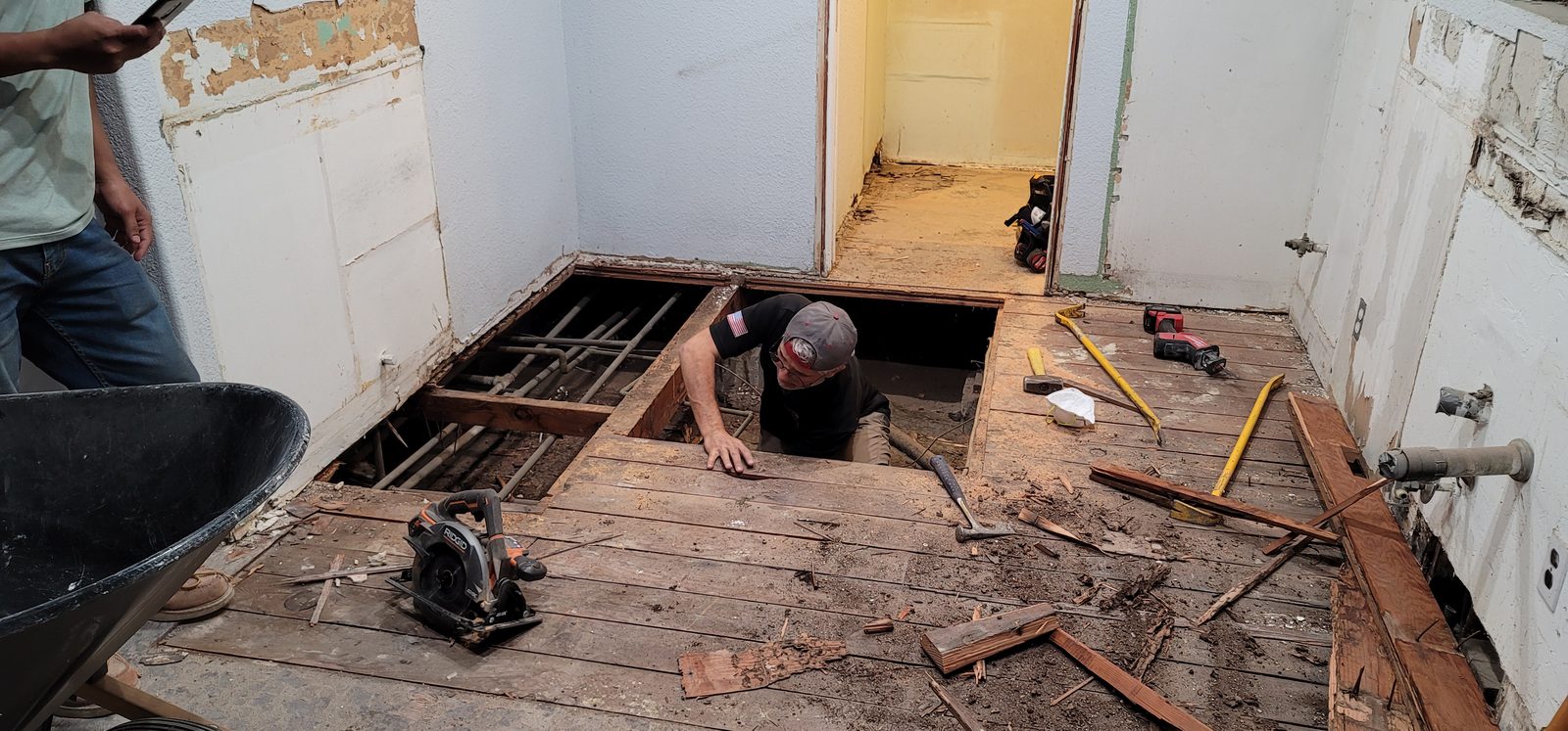 Subfloor removed during a Fullerton whole-home remodel, showing the original plank subfloor and galvanized plumbing beneath the kitchen