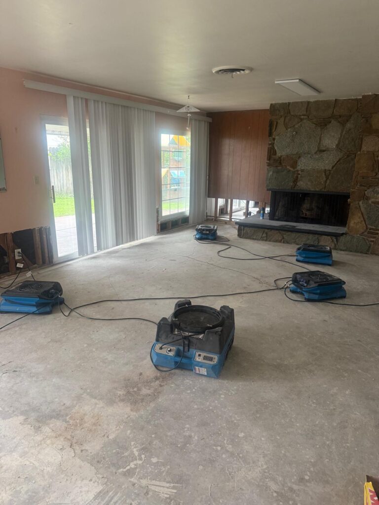 Air movers drying a living room with a stone fireplace after water damage